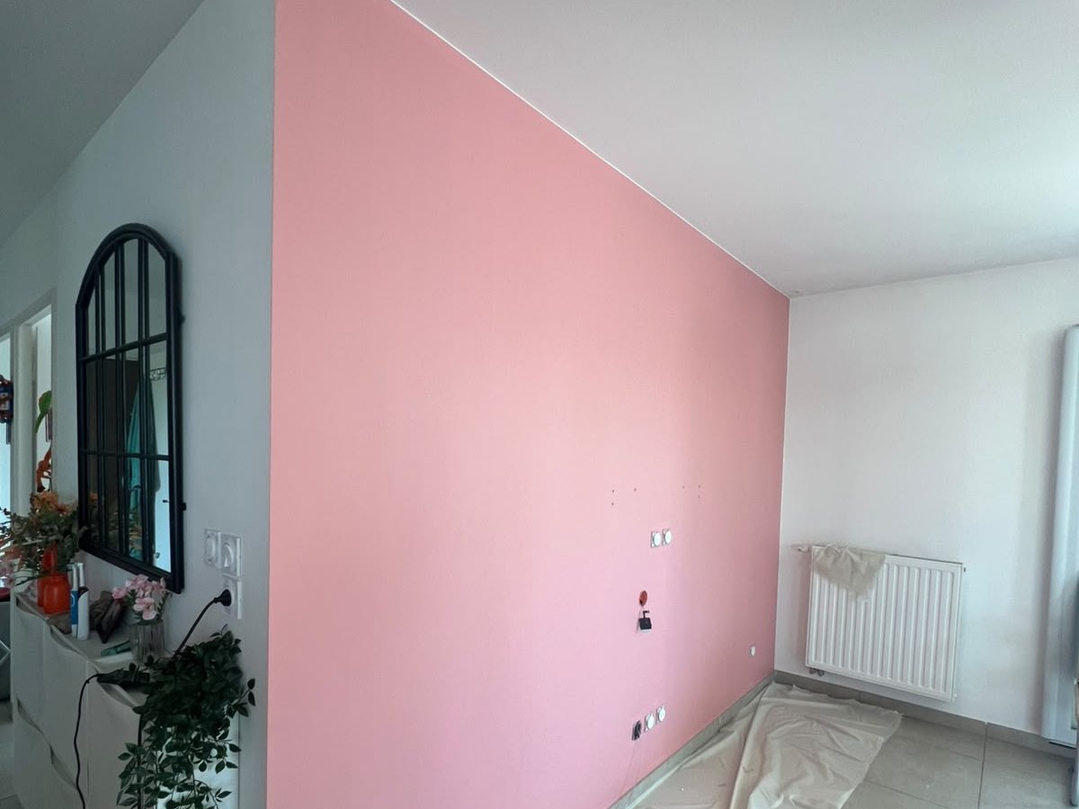 Mur peint en rose dans une pièce, sol encore protégé par une bâche